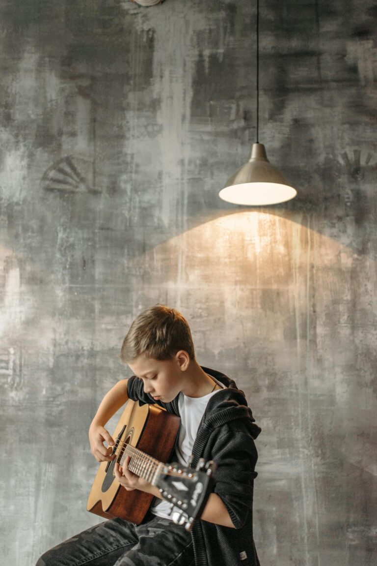 Caucasian boy playing acoustic guitar in a cozy indoor setting under soft lighting.