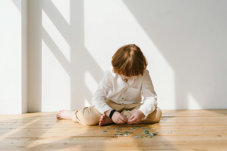 Child sitting on wooden floor concentrating on puzzle pieces, bathed in warm natural light.