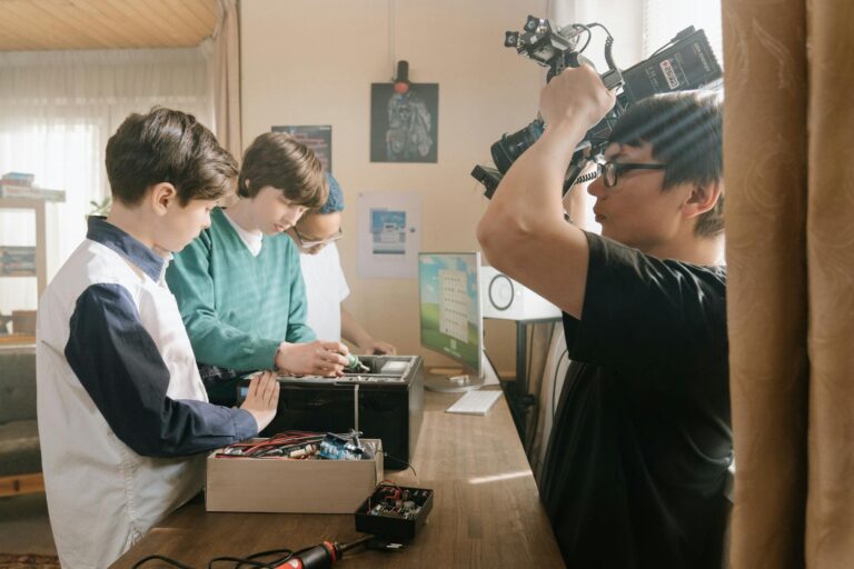 Group of young boys being filmed while working on a tech project with electronic gadgets indoors.