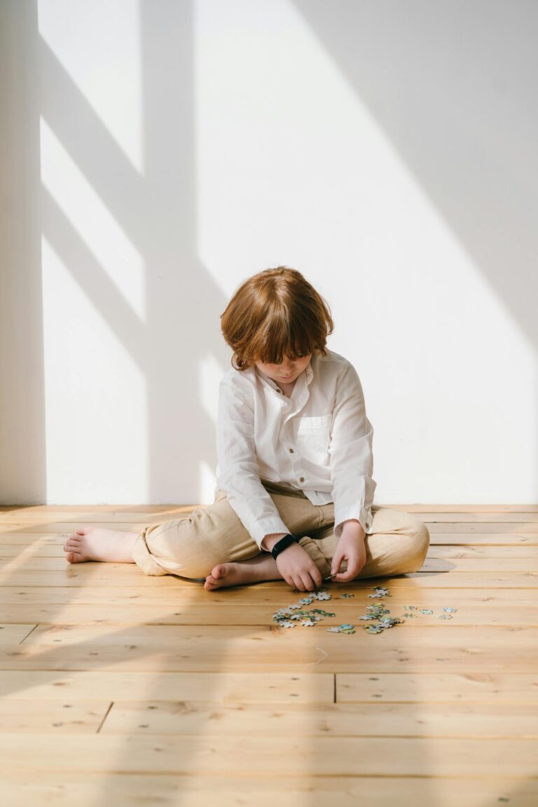 Young boy focuses on assembling a puzzle on wooden floor indoors.